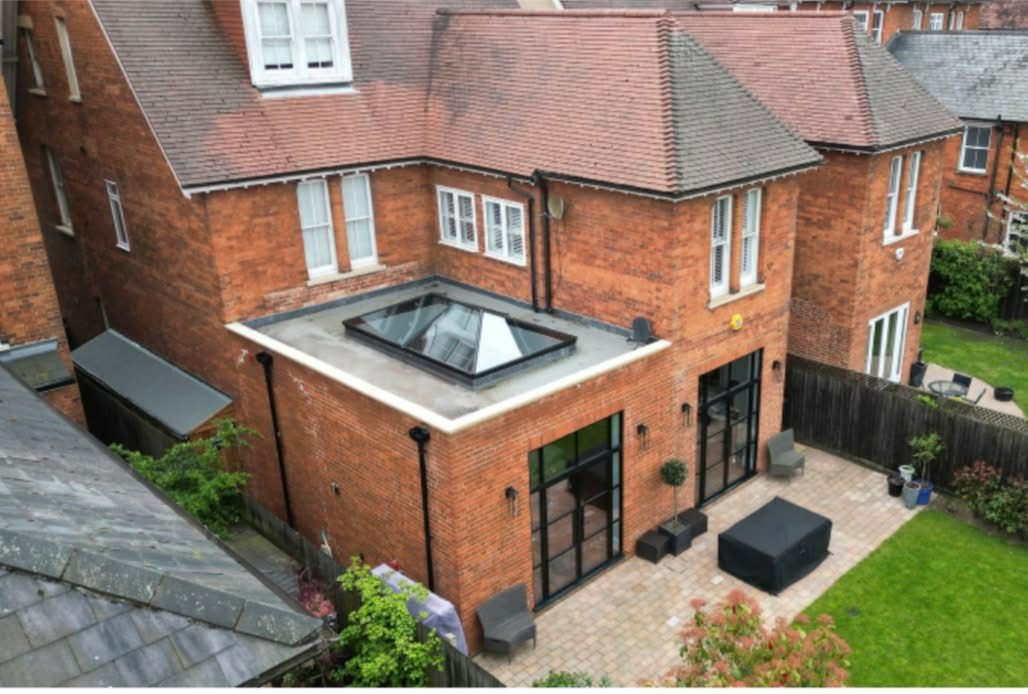 An aerial view of the completed traditional orangery extension in Bedford, featuring a large roof lantern and black Crittal-style doors leading to a new patio.