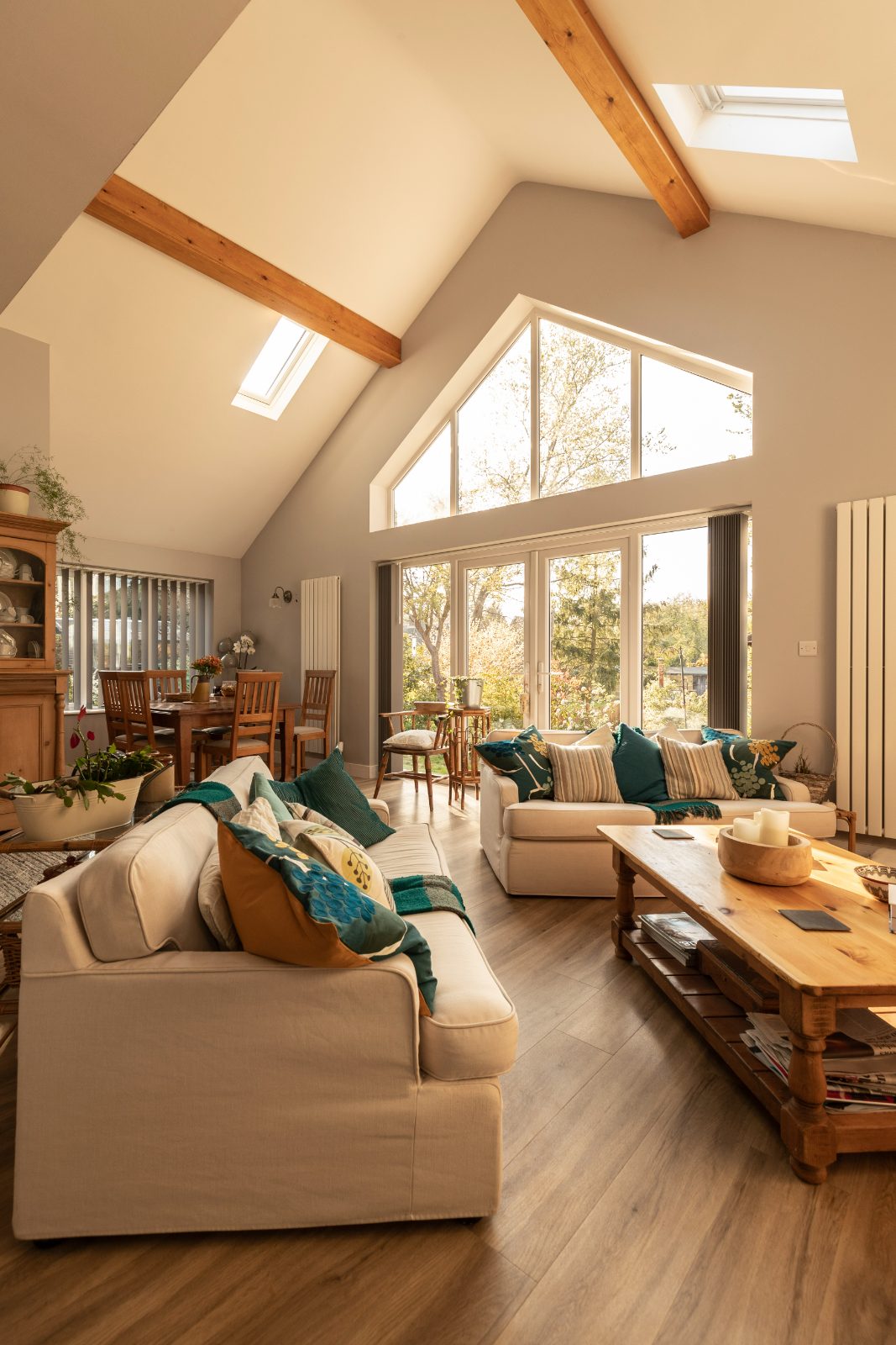 Spacious, light-filled living area with vaulted ceiling, exposed wooden beams, and large windows looking out onto a garden.