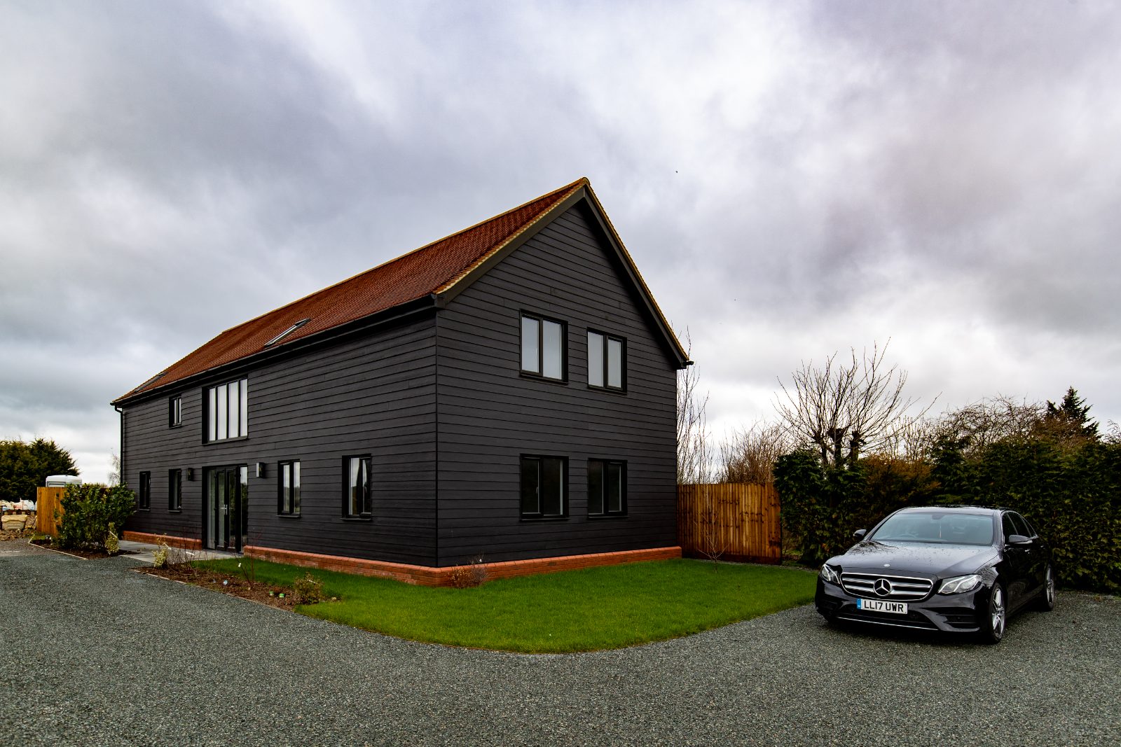 Exterior view of a modern barn-style new build home in Biggleswade with dark timber cladding and a red tiled roof.